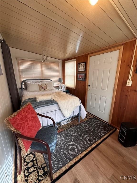 bedroom featuring wood ceiling, wooden walls, an inviting chandelier, and wood finished floors