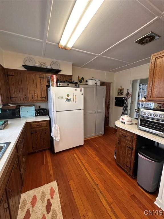 kitchen with a toaster, visible vents, dark wood-type flooring, freestanding refrigerator, and light countertops