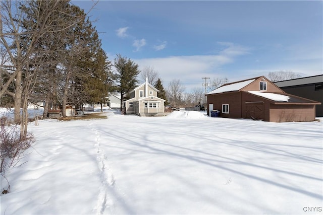 snowy yard featuring an outbuilding, a detached garage, and a barn