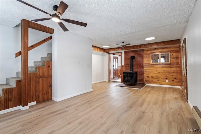 unfurnished living room with stairway, a wood stove, wood walls, a textured ceiling, and wood finished floors