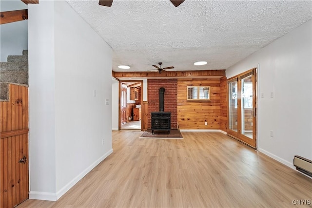 unfurnished living room with a wood stove, light wood-style flooring, a ceiling fan, and a textured ceiling