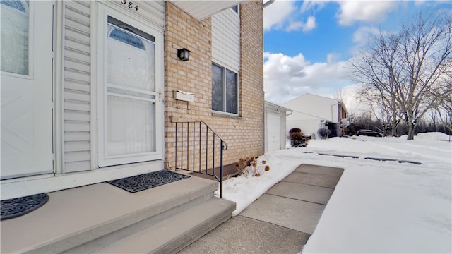 snow covered property entrance with a garage and brick siding