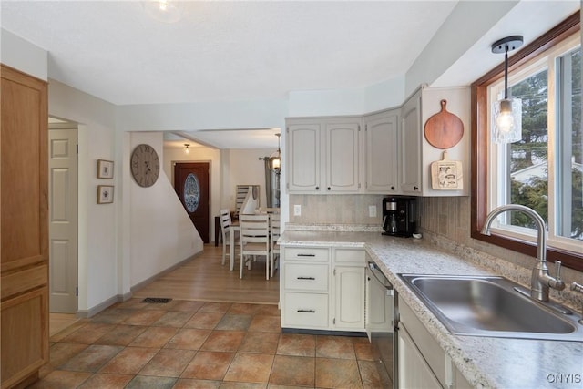 kitchen featuring dishwasher, light countertops, backsplash, and a sink