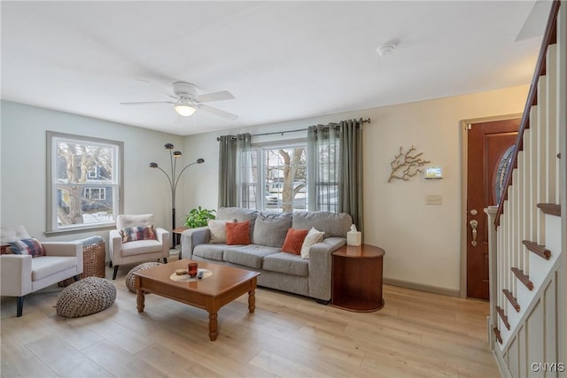 living room featuring ceiling fan, stairway, light wood-type flooring, and baseboards