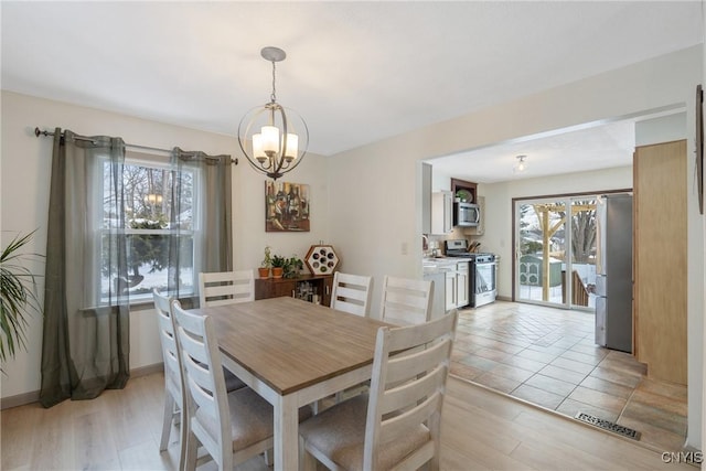 dining space featuring light wood-style floors, visible vents, baseboards, and an inviting chandelier