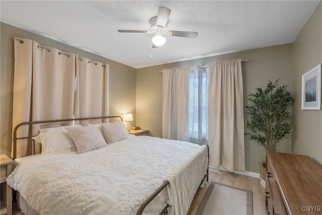 bedroom with a textured ceiling, light wood-style flooring, and a ceiling fan