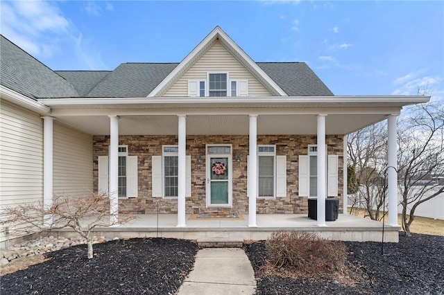 view of exterior entry with stone siding, a shingled roof, and covered porch