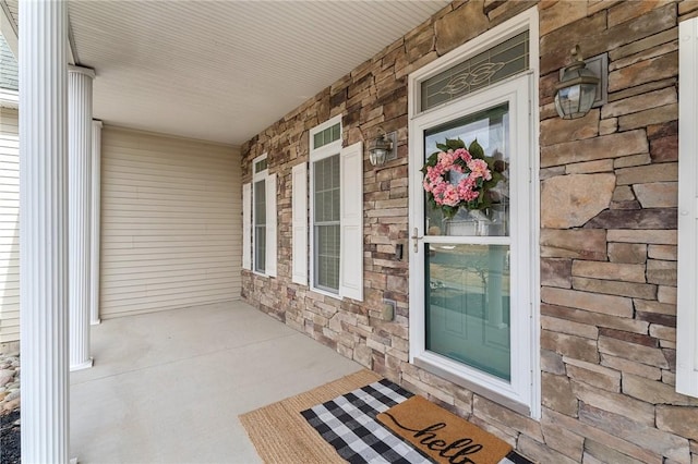 doorway to property featuring stone siding, a porch, and brick siding