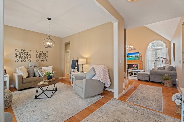 living room featuring lofted ceiling, wood finished floors, baseboards, and an inviting chandelier