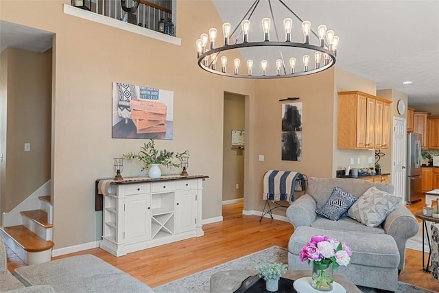 living area featuring baseboards, an inviting chandelier, stairs, and light wood-style floors