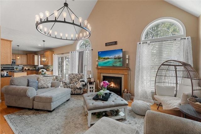 living room featuring light wood-style floors, a lit fireplace, high vaulted ceiling, and an inviting chandelier