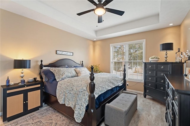 bedroom with ceiling fan, a raised ceiling, light wood-style flooring, and baseboards