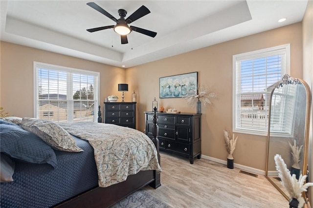 bedroom featuring a tray ceiling, visible vents, light wood-style floors, a ceiling fan, and baseboards