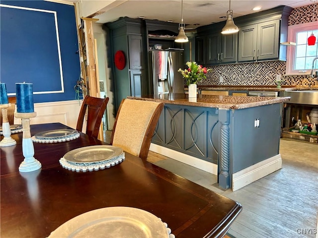 kitchen with light wood finished floors, stainless steel fridge, pendant lighting, open shelves, and backsplash