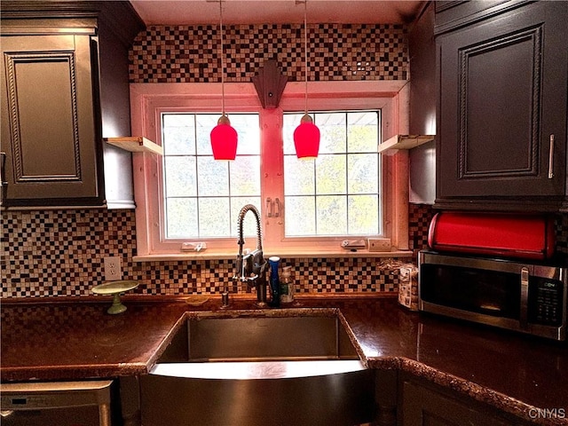 kitchen with tasteful backsplash, stainless steel microwave, dark countertops, and a sink