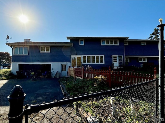 rear view of property with an attached garage, fence, and aphalt driveway