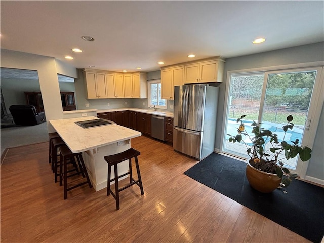 kitchen featuring recessed lighting, stainless steel appliances, a breakfast bar, wood finished floors, and light countertops