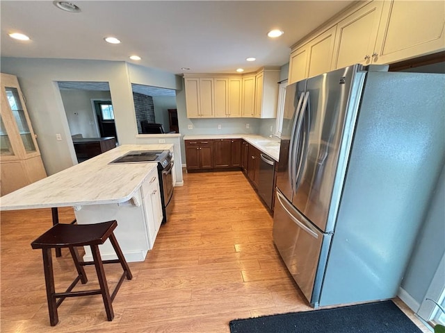 kitchen with recessed lighting, appliances with stainless steel finishes, a sink, light wood-type flooring, and a kitchen bar