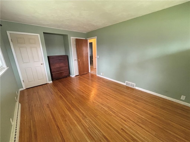 unfurnished bedroom featuring baseboards, visible vents, a baseboard radiator, wood finished floors, and a closet