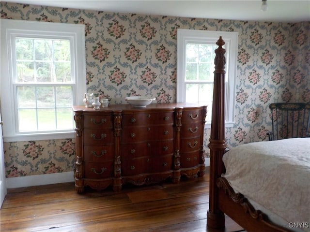 bedroom featuring wood finished floors, baseboards, and wallpapered walls