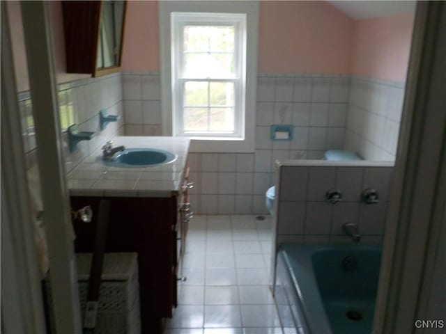 bathroom with toilet, a bathing tub, tile patterned flooring, vanity, and tile walls