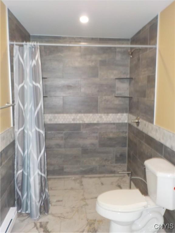 full bathroom featuring toilet, marble finish floor, a tile shower, and tile walls