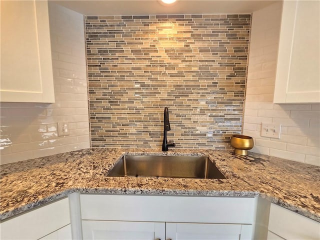 kitchen with light stone countertops, backsplash, white cabinets, and a sink