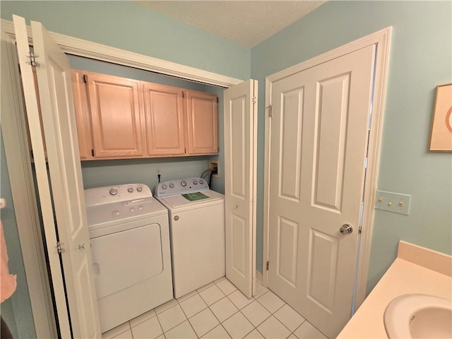 laundry area featuring light tile patterned floors, a textured ceiling, a sink, cabinet space, and washer and clothes dryer