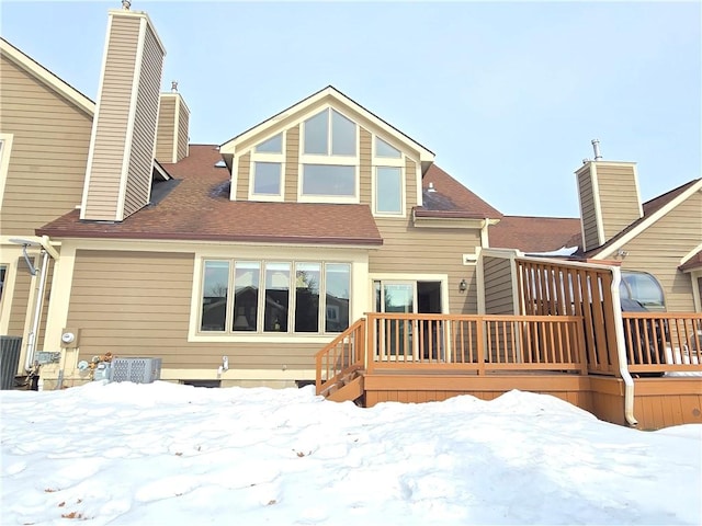 snow covered house with roof with shingles, a chimney, and a wooden deck