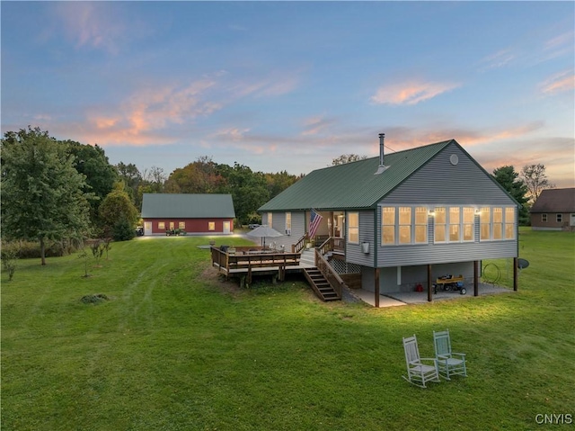 back of property with a lawn, driveway, metal roof, a wooden deck, and stairs