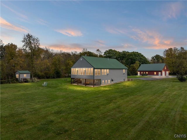 23000 County Route 57, Lyme, NY 13693 - back of property at dusk with a detached garage, a yard, driveway, and an outbuilding
