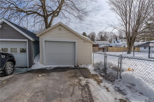 snow covered garage featuring a gate, a detached garage, driveway, and fence