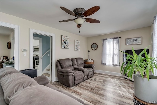 living area featuring stairs, ceiling fan, baseboards, and wood finished floors