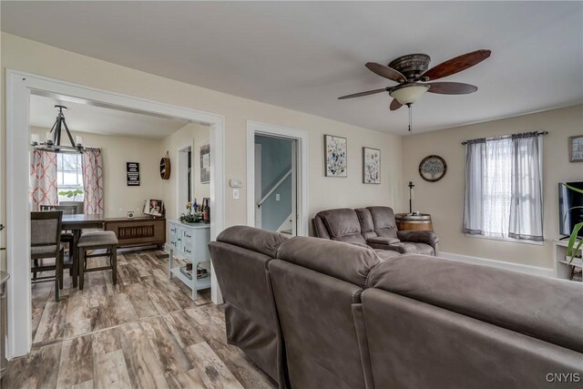 living room featuring ceiling fan with notable chandelier, wood finished floors, and baseboards