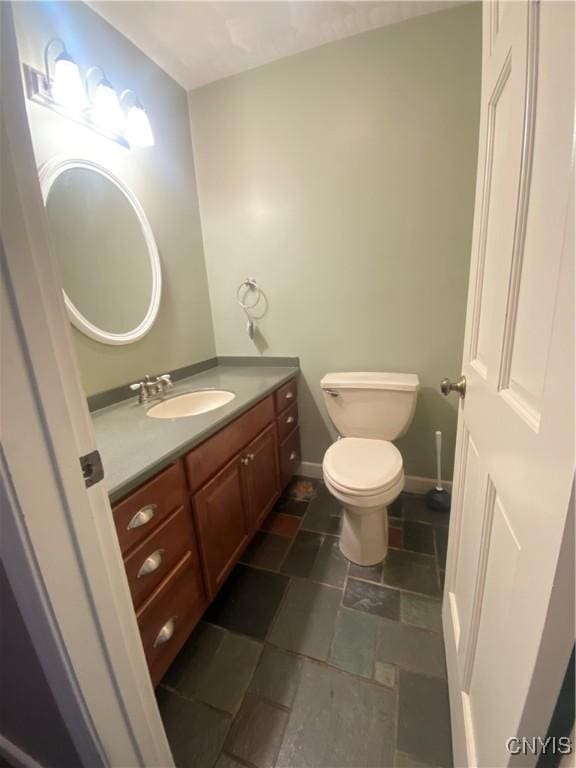 half bath featuring stone finish floor, vanity, toilet, and baseboards