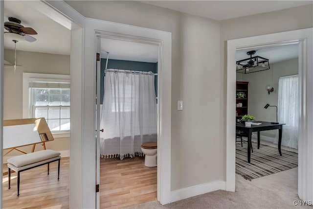 corridor with light carpet, light wood finished floors, and baseboards