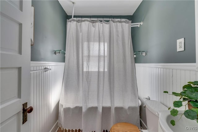 full bathroom with toilet, a wainscoted wall, and curtained shower