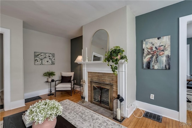 living area featuring a brick fireplace, wood finished floors, visible vents, and baseboards