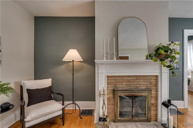 living area with a brick fireplace, wood finished floors, visible vents, and baseboards