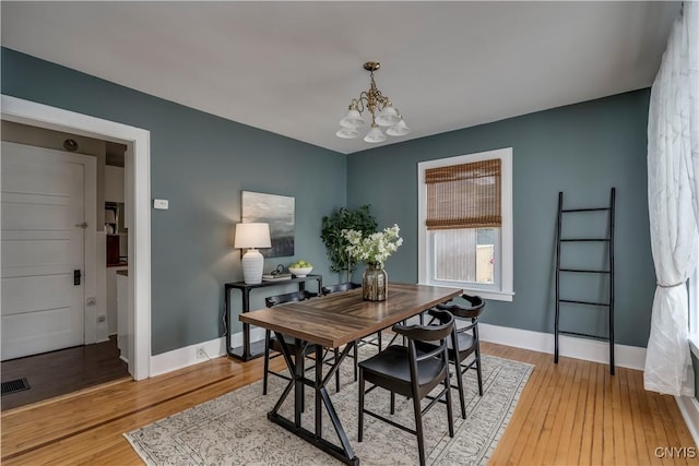 dining room featuring baseboards, light wood-type flooring, visible vents, and a notable chandelier