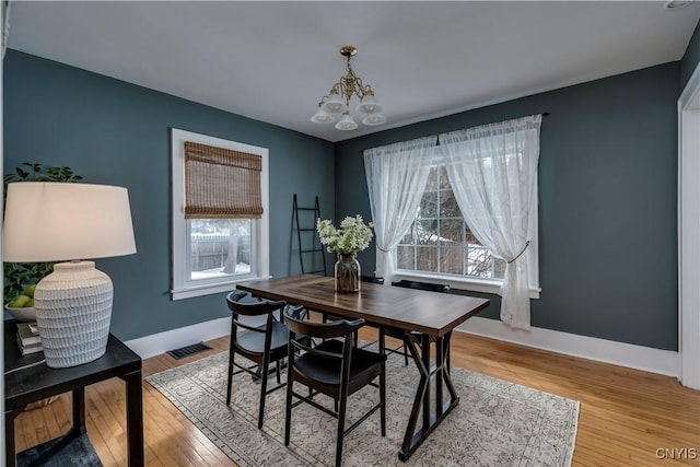 dining space featuring baseboards, light wood finished floors, visible vents, and a notable chandelier