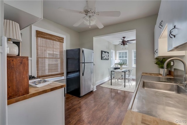 kitchen featuring a sink, wood counters, white cabinets, freestanding refrigerator, and dark wood-style floors