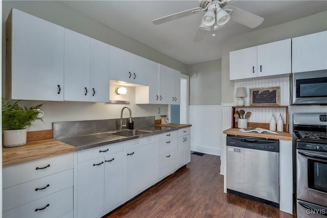 kitchen with a wainscoted wall, appliances with stainless steel finishes, dark wood-type flooring, stainless steel counters, and a sink