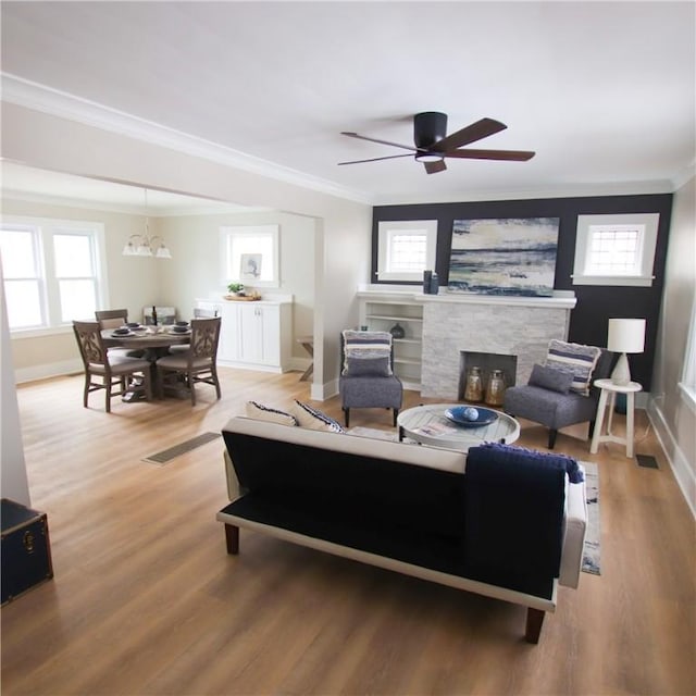 living room featuring baseboards, a ceiling fan, ornamental molding, light wood-type flooring, and a fireplace