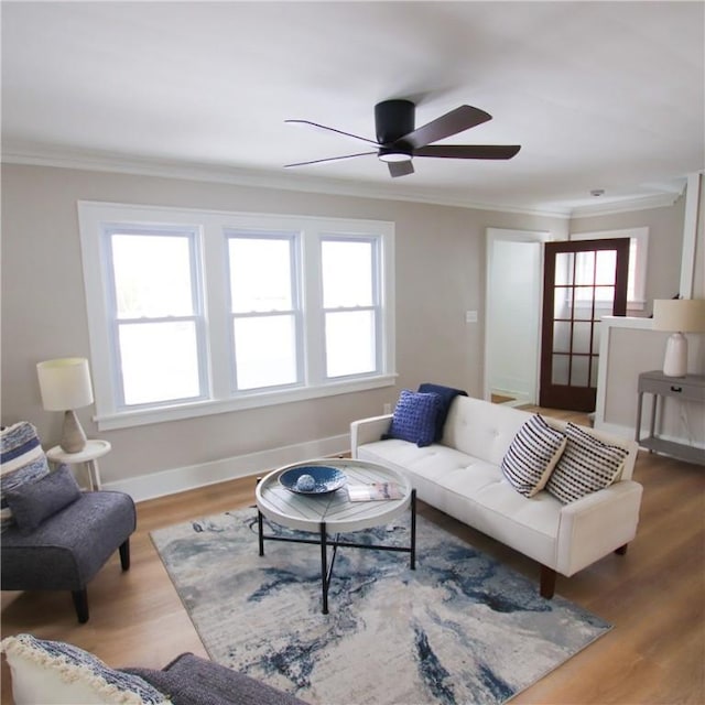 living area featuring ceiling fan, crown molding, baseboards, and wood finished floors