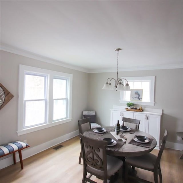 dining room with light wood finished floors, visible vents, and crown molding