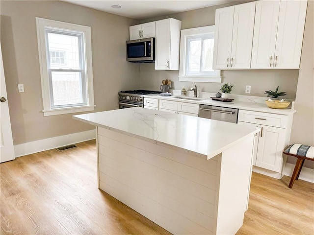 kitchen featuring light wood finished floors, appliances with stainless steel finishes, white cabinets, and a sink