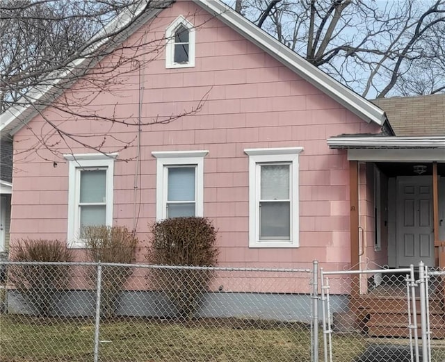 view of side of home featuring a fenced front yard, a gate, and a shingled roof