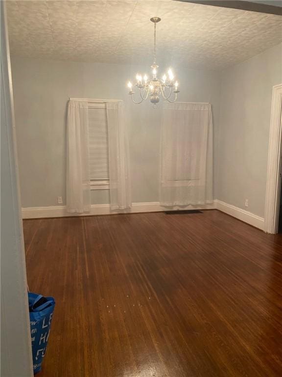 spare room with baseboards, a textured ceiling, a chandelier, and wood finished floors