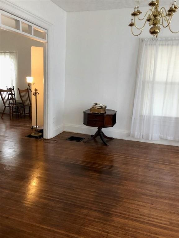 empty room with a chandelier, dark wood finished floors, and baseboards